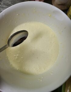 常温のクリームチーズに砂糖、小麦粉、全卵を入れてハンドミキサーで混ぜたものが入った白いボウルにレモン汁を足したところ