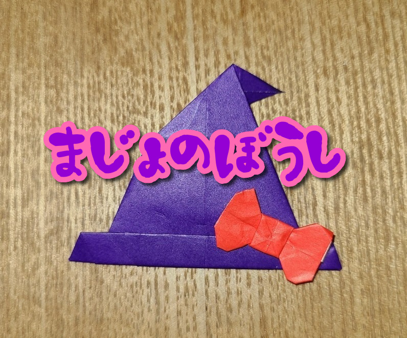 紫の折り紙で作った魔女の帽子に赤いリボンがついている